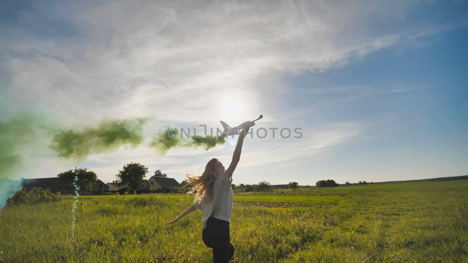 A young girl with a toy airplane smokes colorful smoke on a summer evening