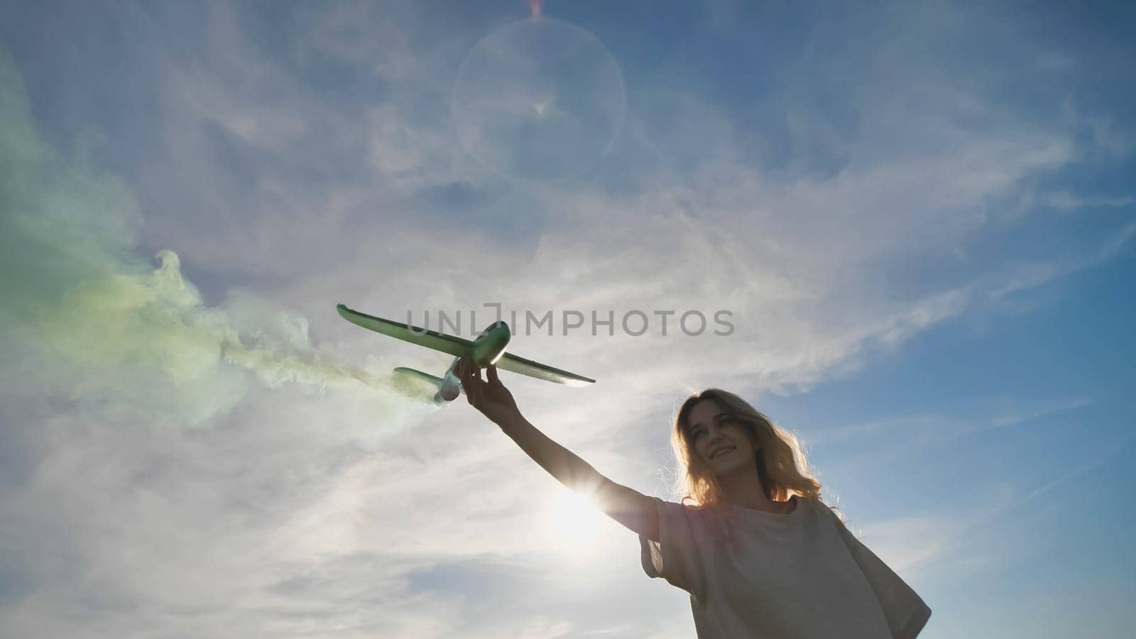 A young girl with a toy airplane smokes colorful smoke on a summer evening