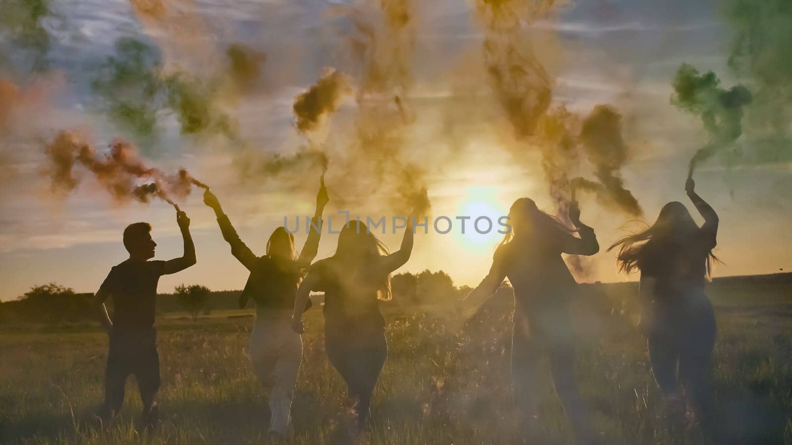 Happy friends waving colorful smoke at sunset