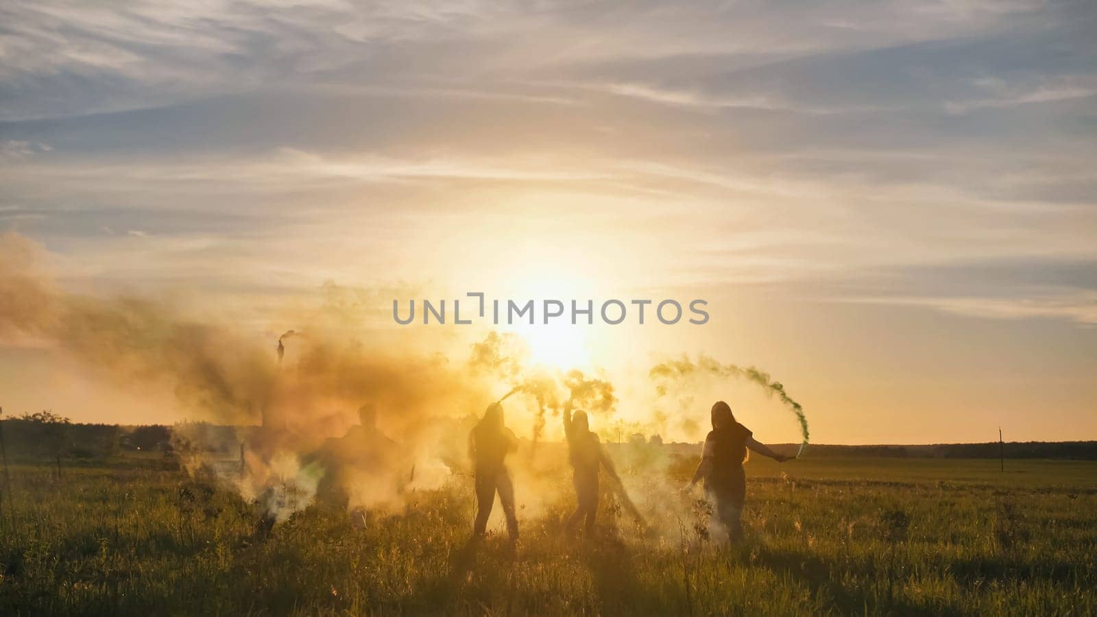 Happy friends waving colorful smoke at sunset