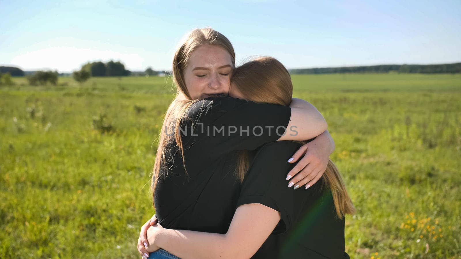Portrait of hugging two twin sisters in the field on a warm summer day.
