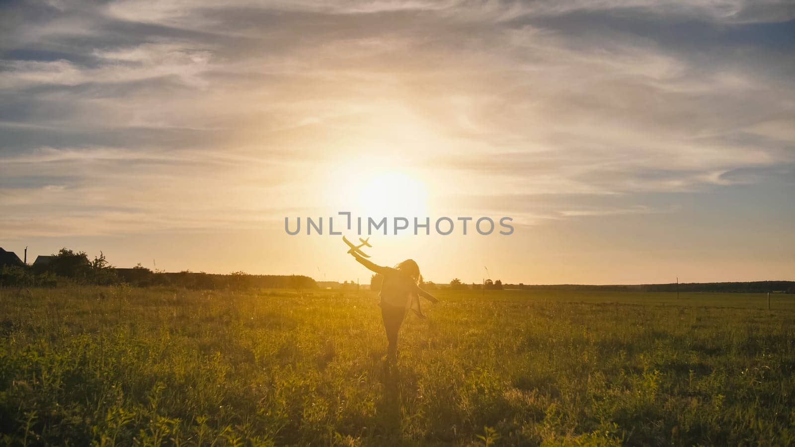 A young girl runs with a toy airplane against the sunset sky