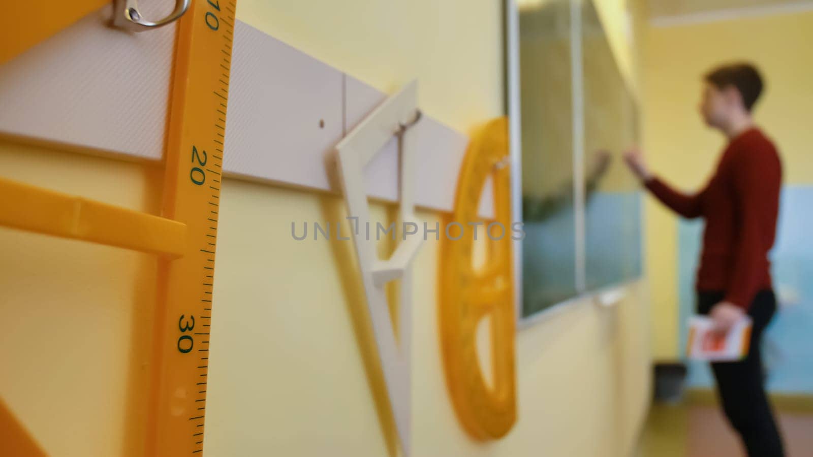 A schoolboy writes on the blackboard during a geometry lesson. Geometry school supplies in the foreground