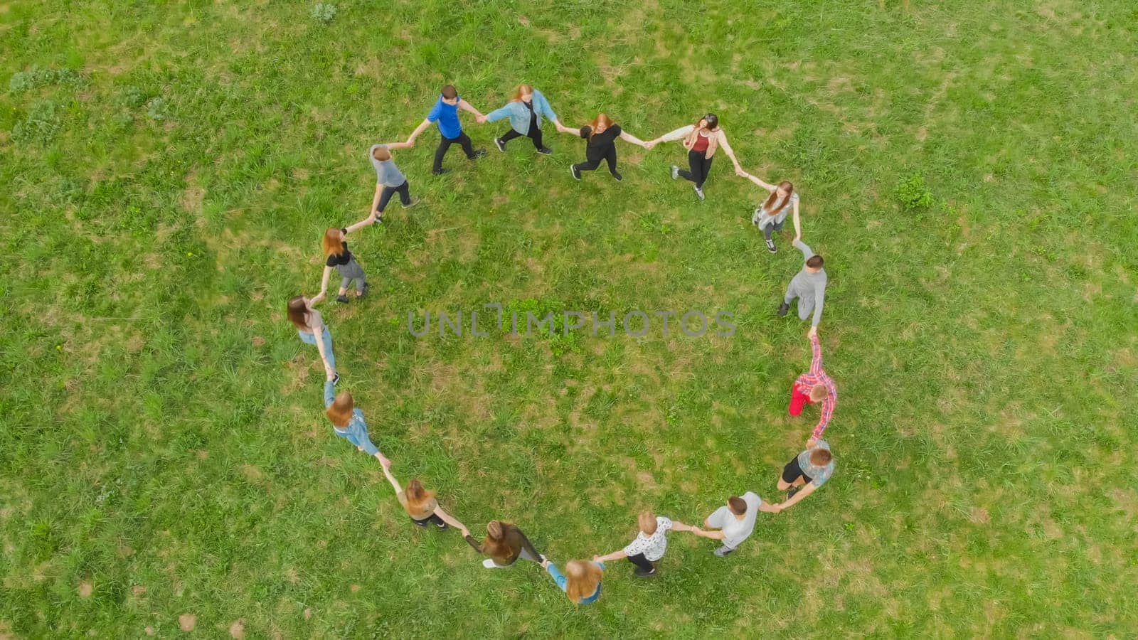Friends in a circle holding hands make a round dance in the field