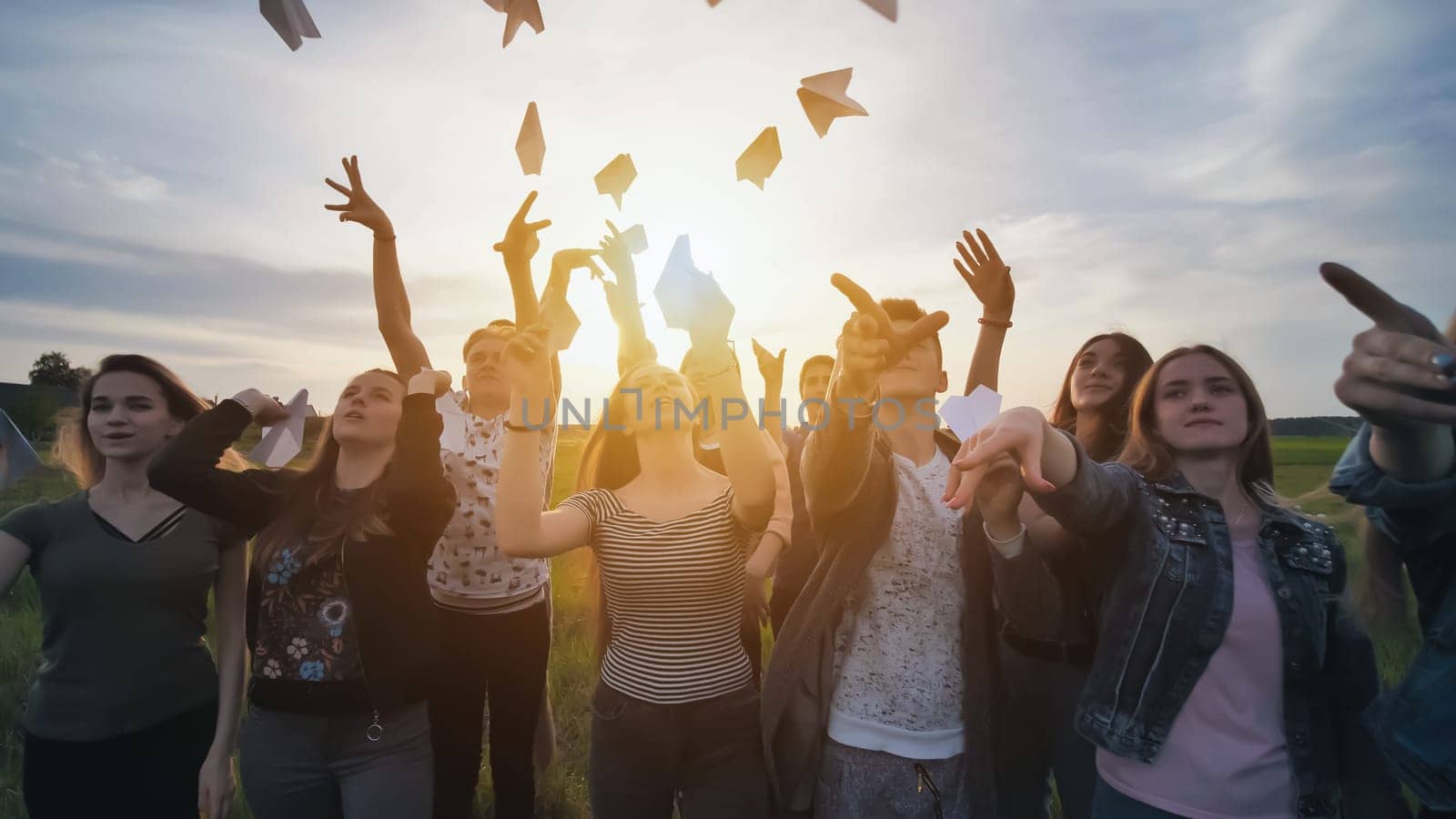 Happy friends launch paper airplanes at sunset