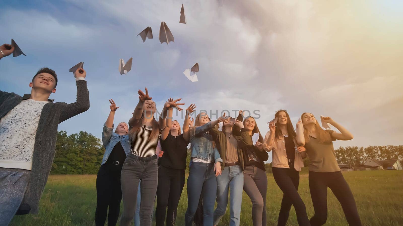 Happy friends launch paper airplanes at sunset