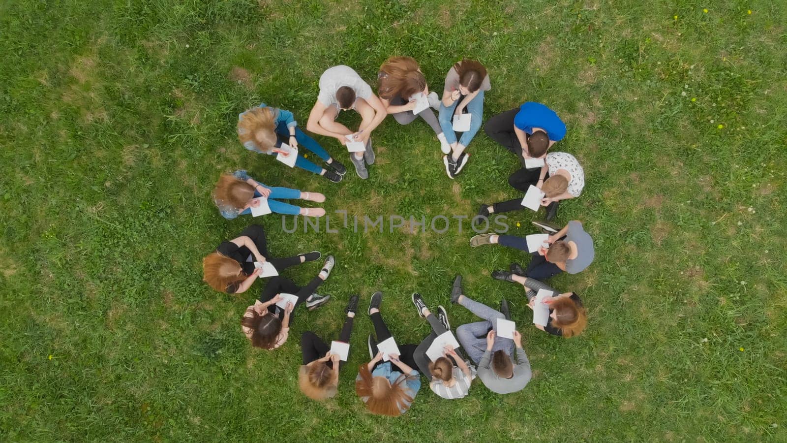 A group of students are sitting in a circle and books on the grass