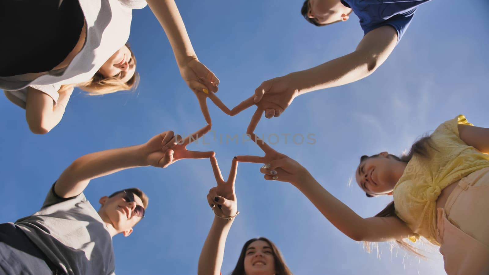 Friends make a star shape from their hands against a blue sky.