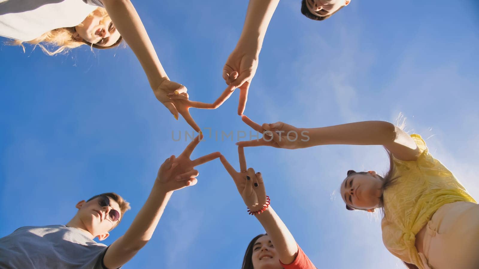 Friends make a star shape from their hands against a blue sky.