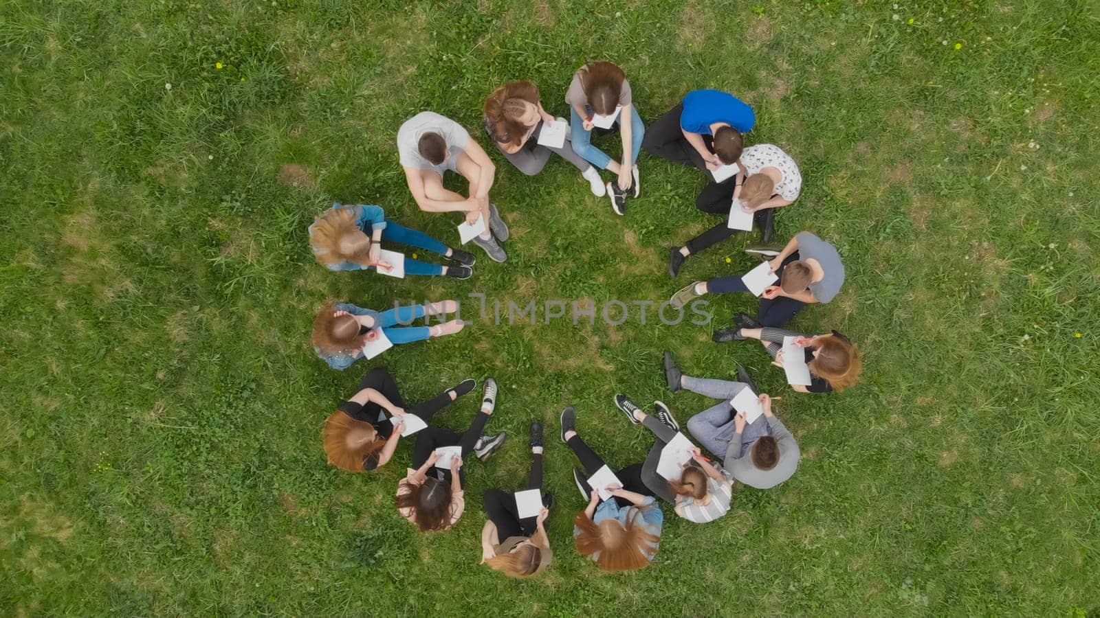 A group of students are sitting in a circle and books on the grass