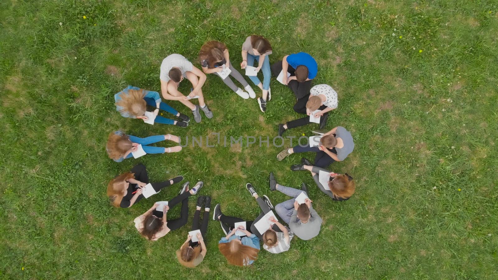 A group of students are sitting in a circle and books on the grass