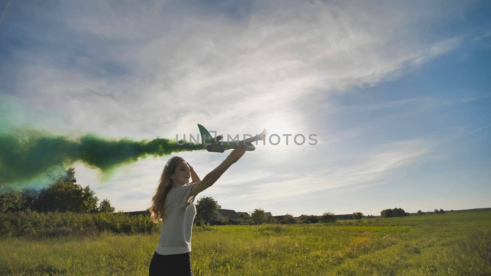 A young girl with a toy airplane smokes colorful smoke on a summer evening