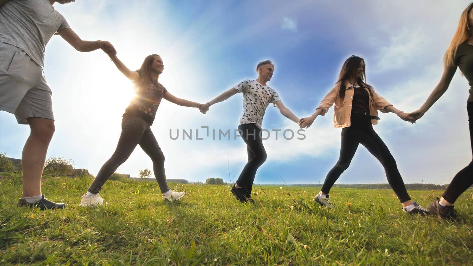 A group of young people lead a round dance holding hands on a summer day. Unity concept