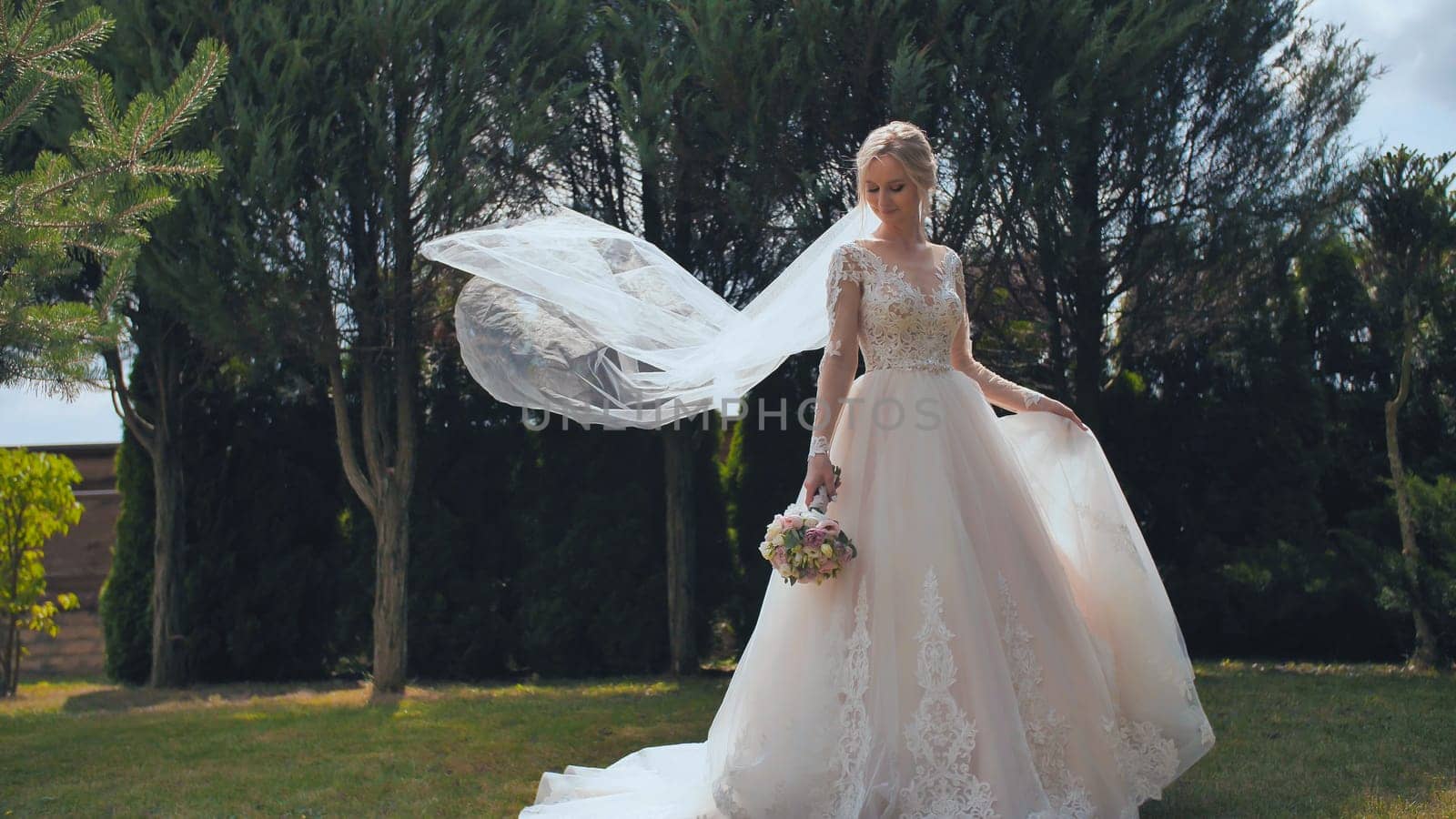 A young bride is standing in a park and her veil is slowly falling her veil is slowly falling.
