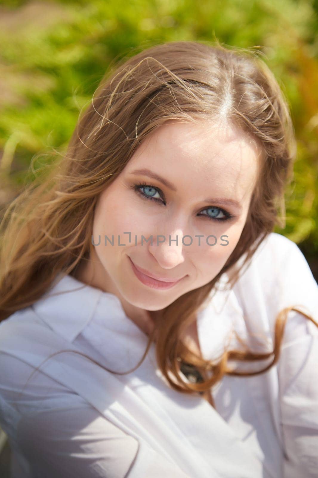 A young woman with blue eyes and brown hair enjoys a sunny day outdoors in a vibrant green environment.