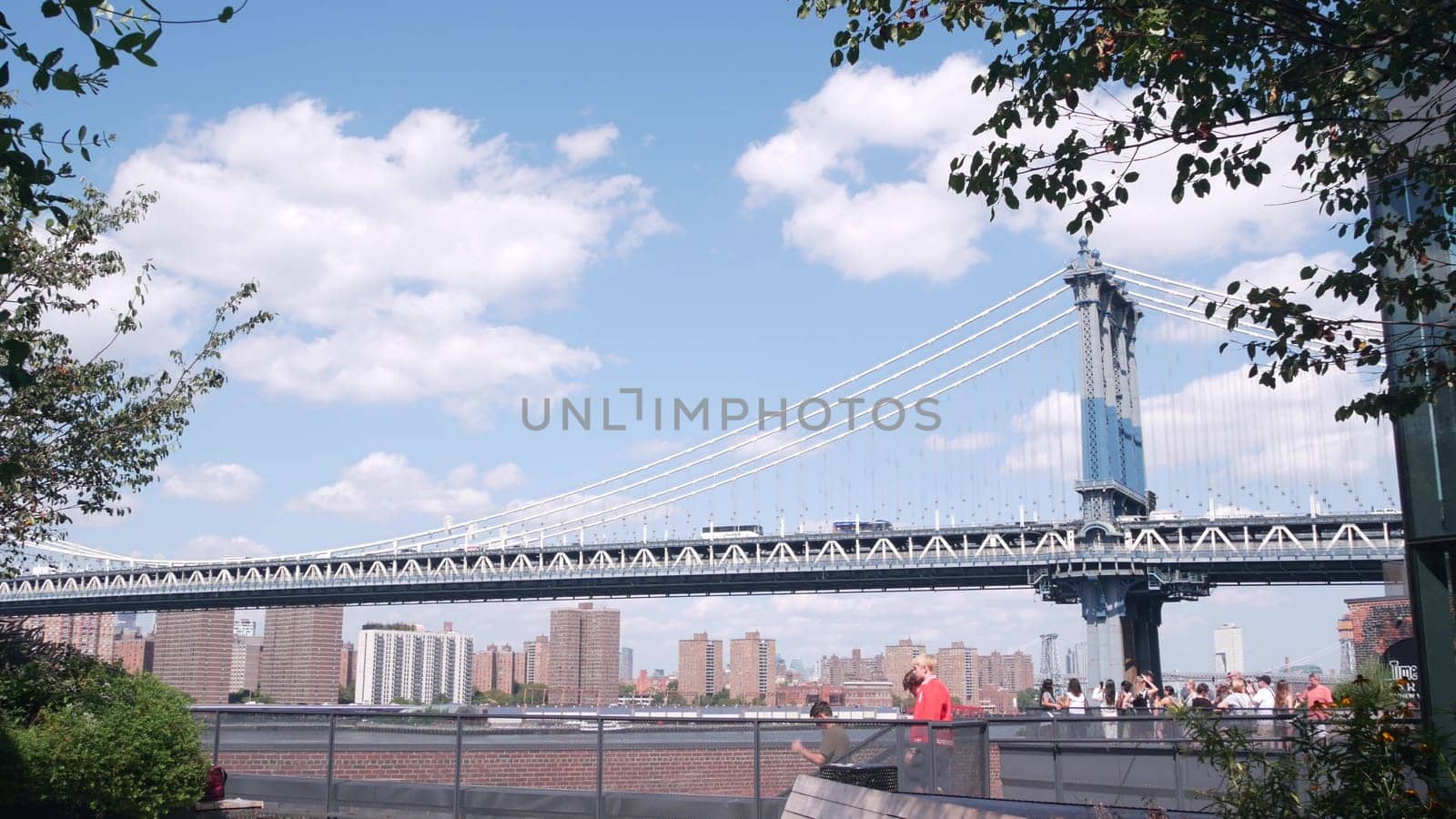 New York City, United States - 30 Aug 2023: Cable-stayed Manhattan Bridge to Brooklyn Dumbo. Bench on Time Out Market rooftop, iconic United States travel destination. People on NYC roof vista point.