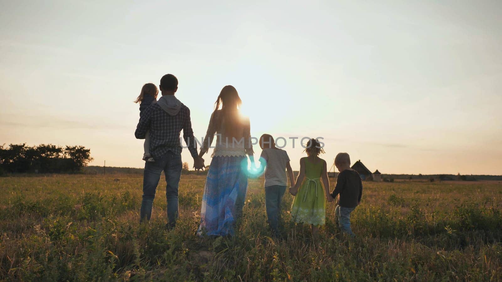 A large family walks along the field at sunset