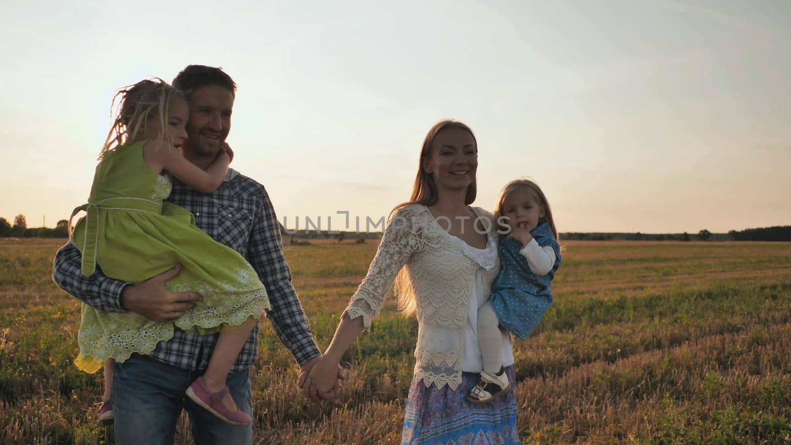 Young parents carry their children in their arms across the field at sunset