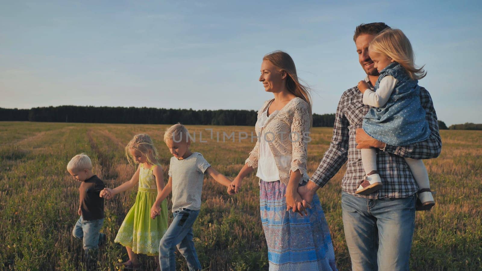 A large family walks along the field at sunset