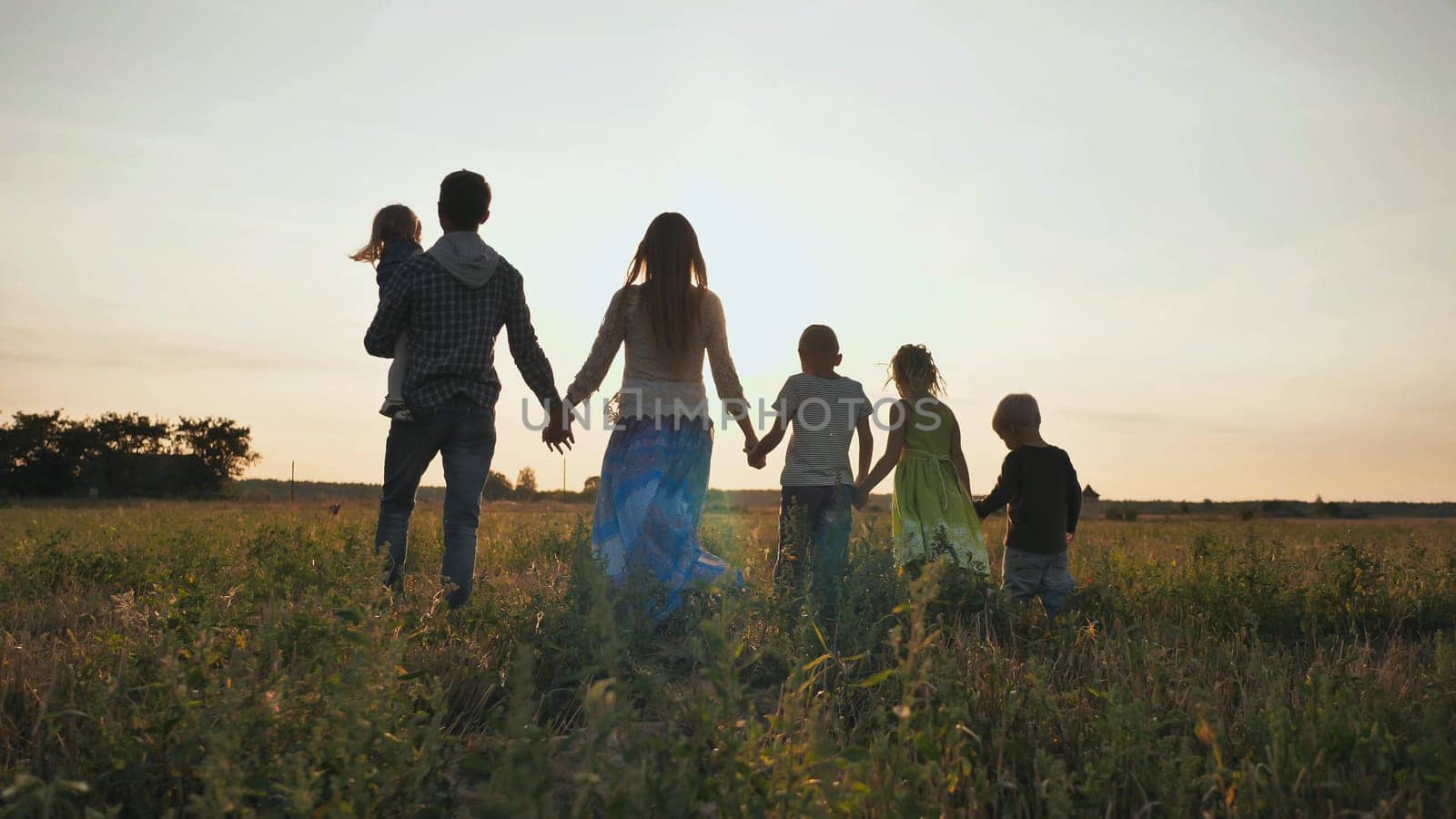 A large family walks along the field at sunset