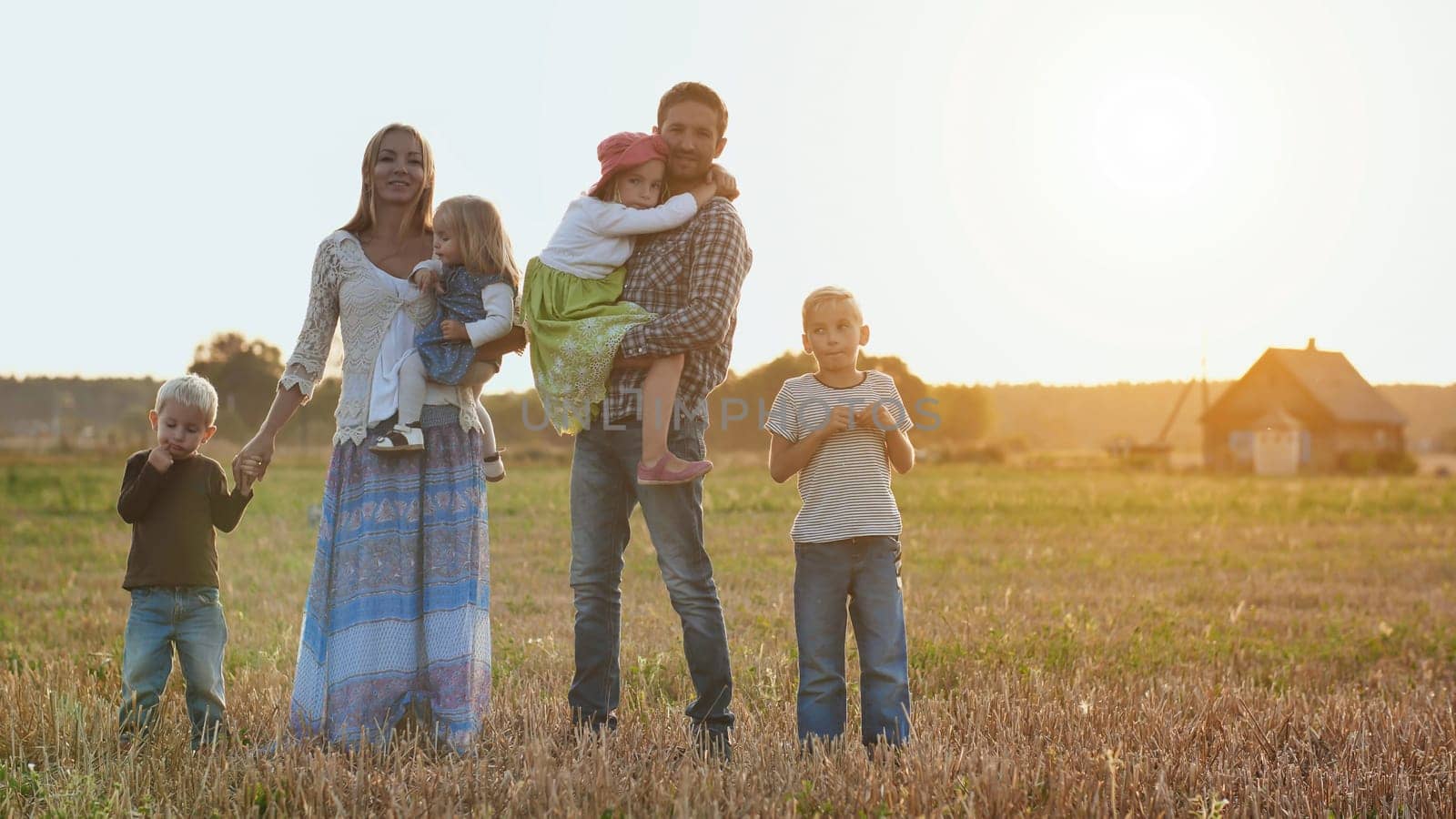 A large family goes on the field in the village during sunset