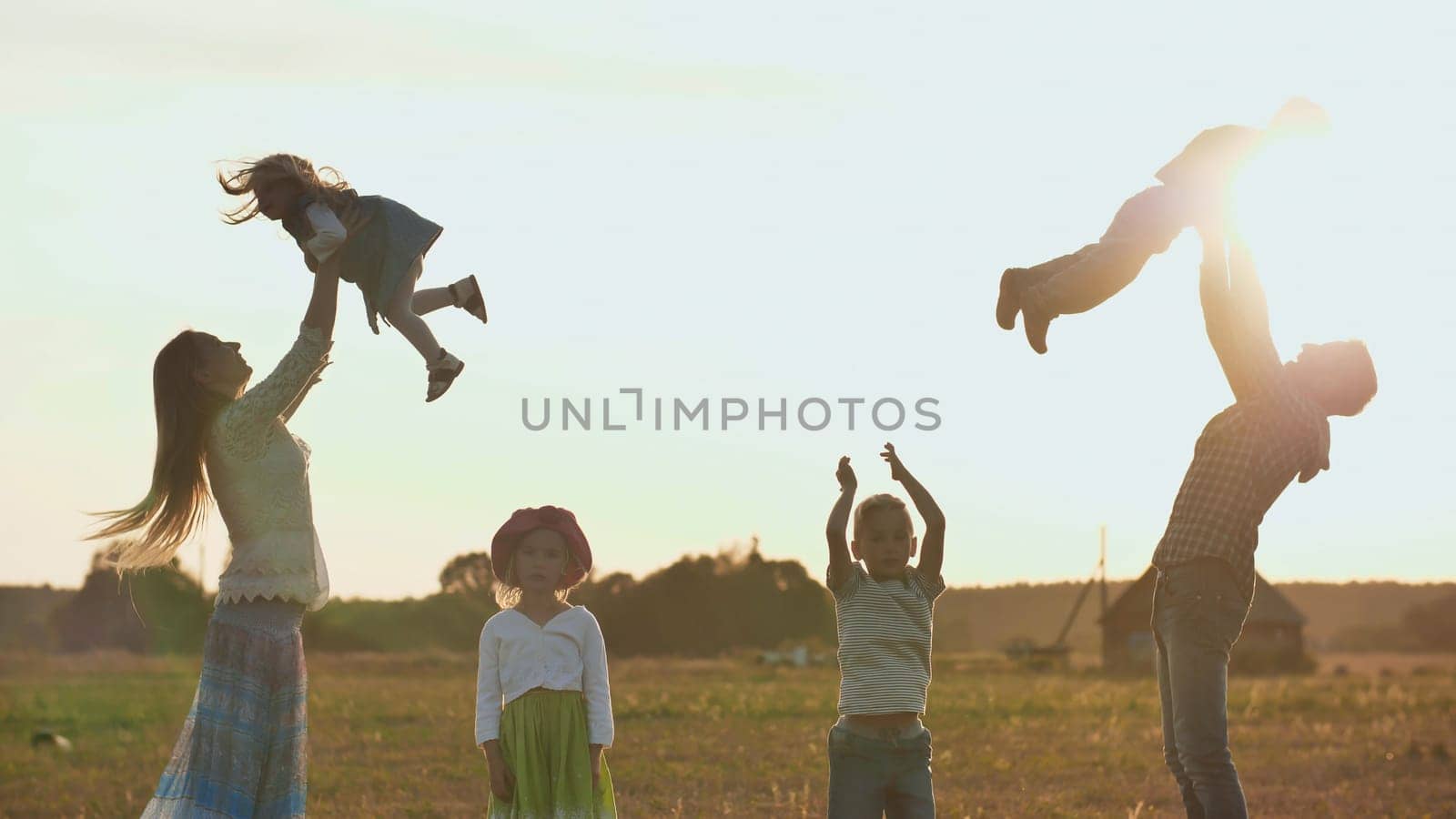 Happy parents tossing their children up on a sunset background. The concept of a happy large family.