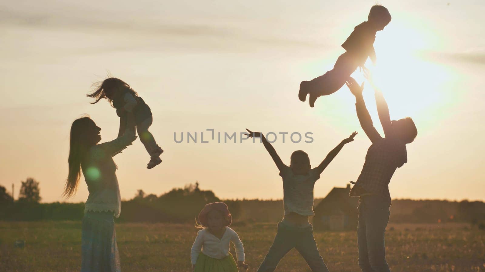 Happy parents tossing their children up on a sunset background. The concept of a happy large family.