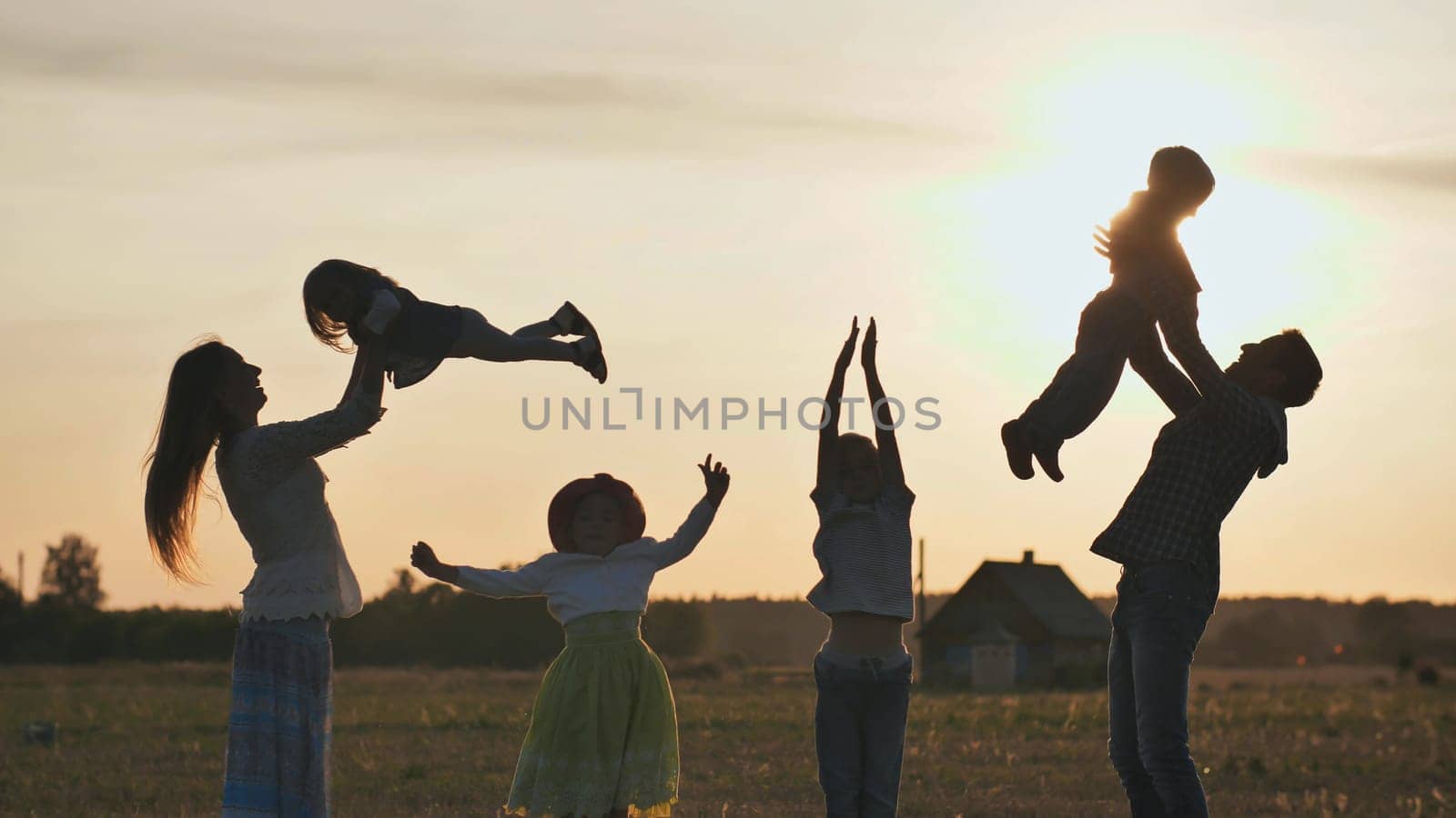 Happy parents tossing their children up on a sunset background. The concept of a happy large family.