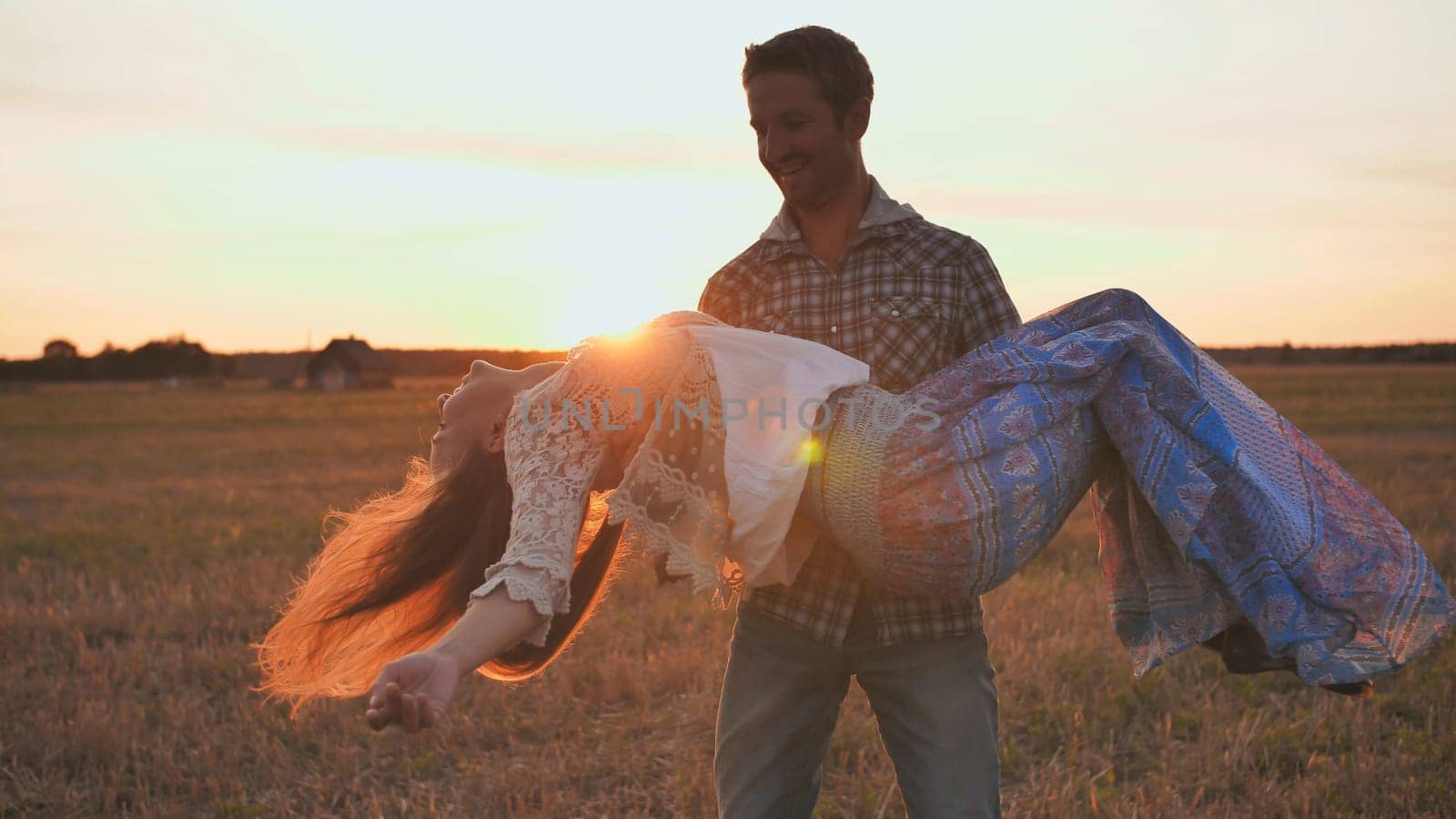 A guy is circling his girlfriend in his arms on a sunset background