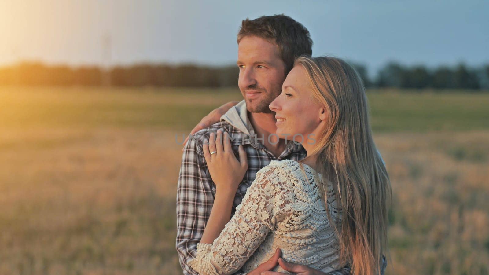 Young husband and wife cuddle at sunset and look towards the sun.