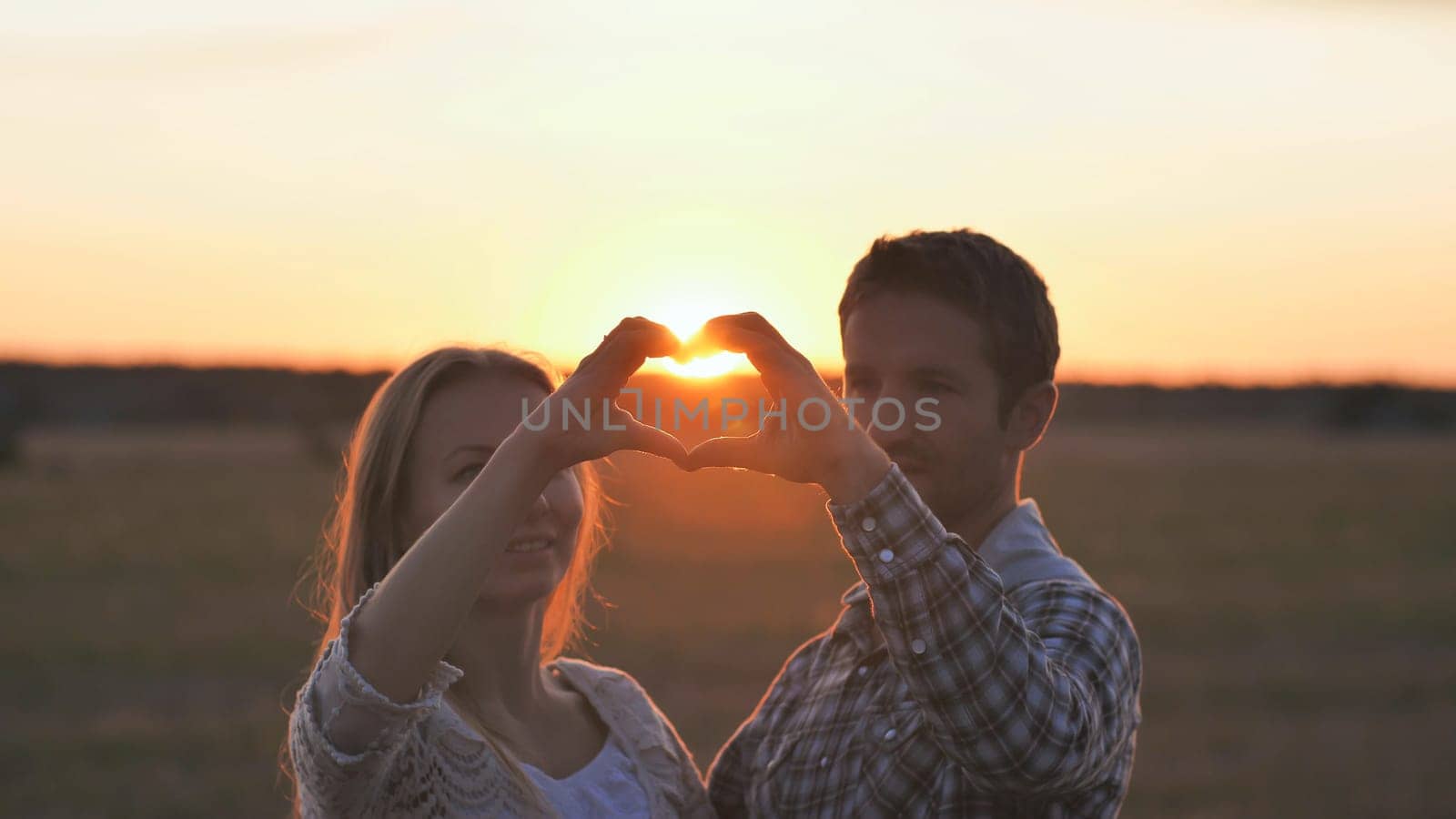Couple making heart shape with hands. Sunset time