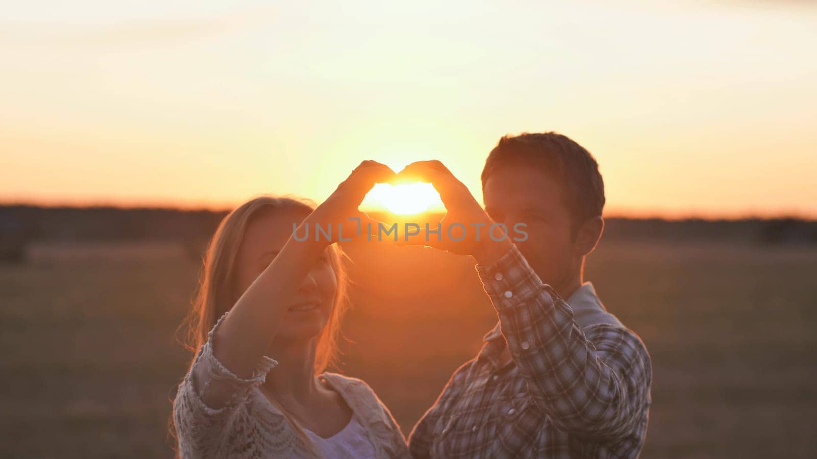 Couple making heart shape with hands. Sunset time