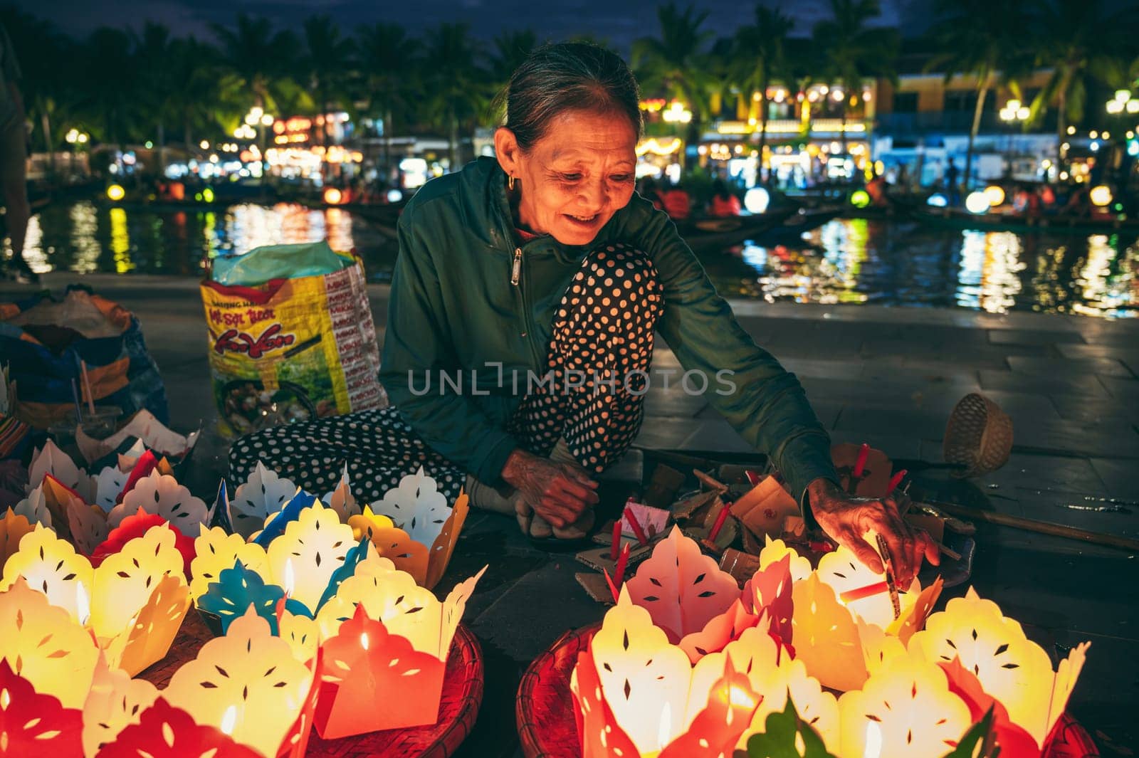 Elderly Vietnamese woman seller sells paper lanterns for a festive festival by river in old town in Hoi An city in Asia. Hoi An, Vietnam - December 1, 2024