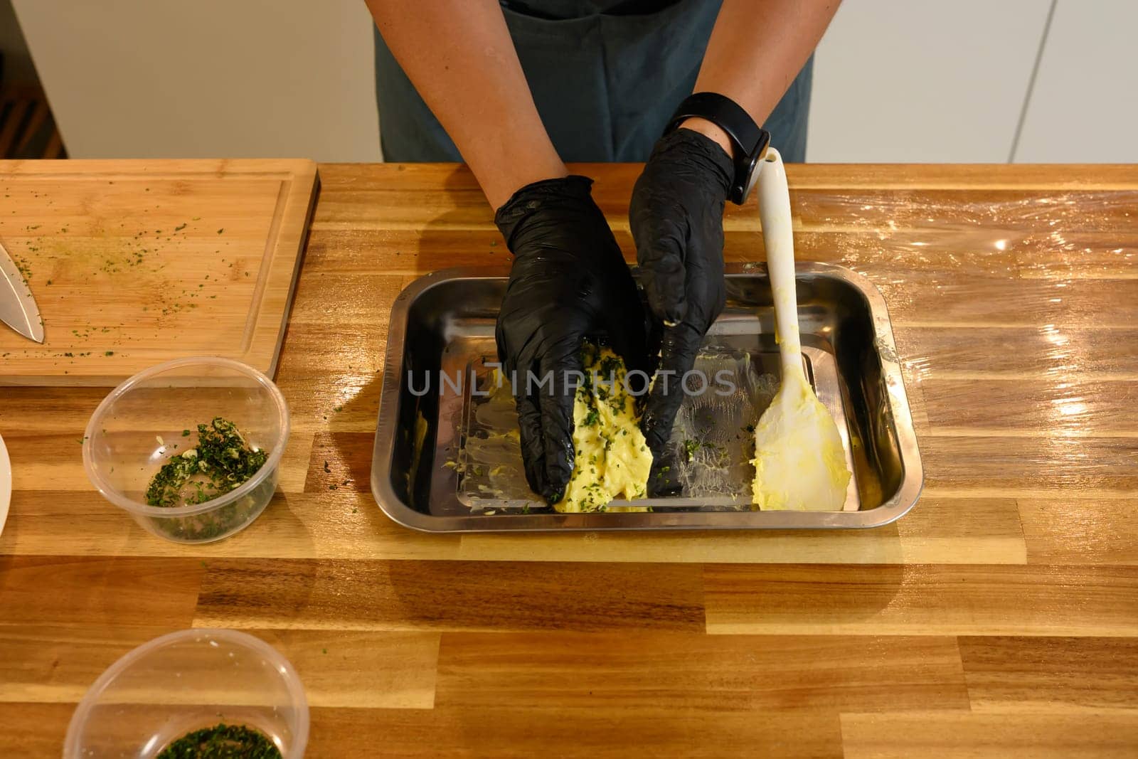 Overhead view of man mixing compound butter with fresh herbs and garlic on kitchen counter.