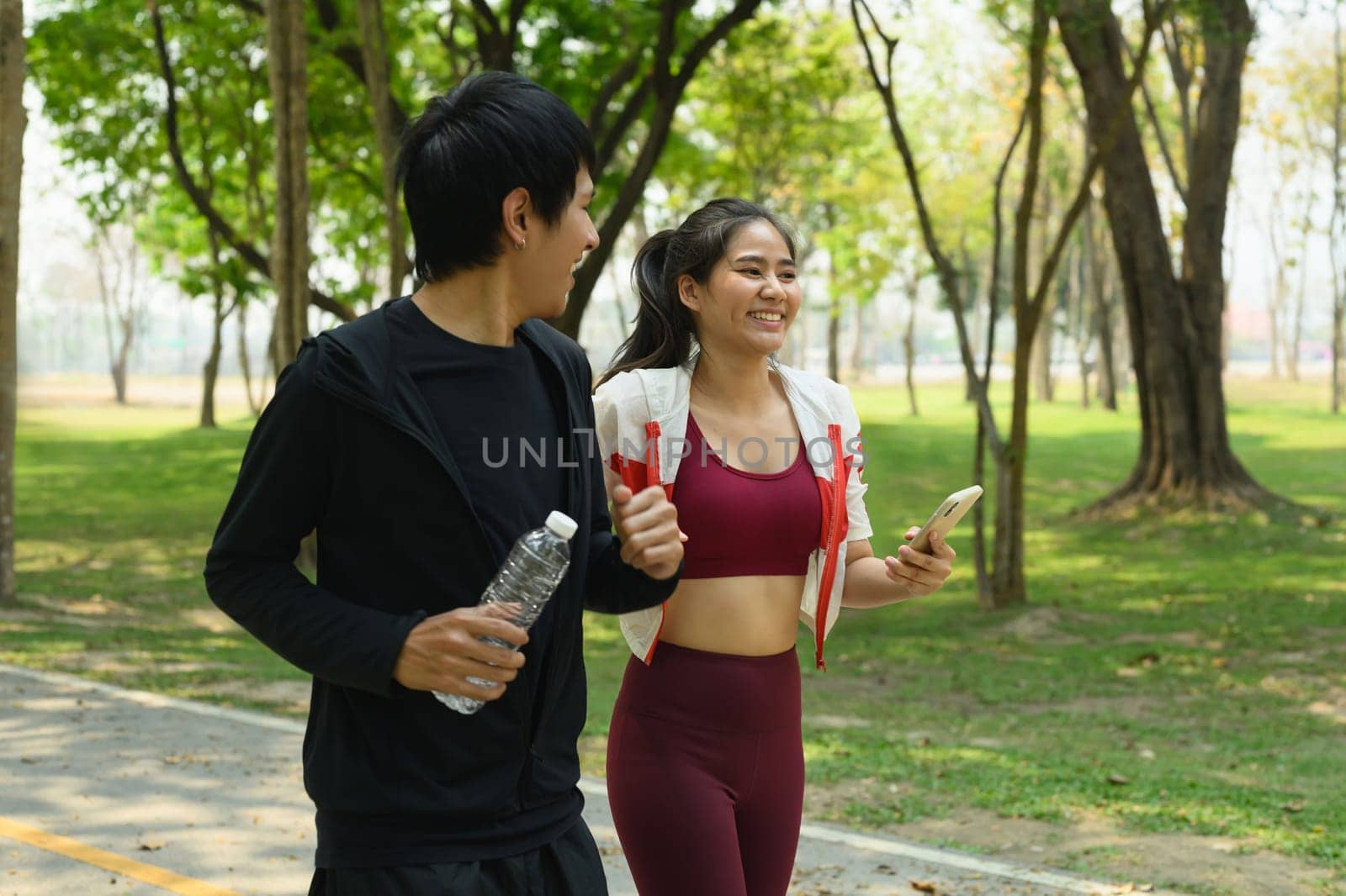 Happy man and woman walking through a green park after workout session.