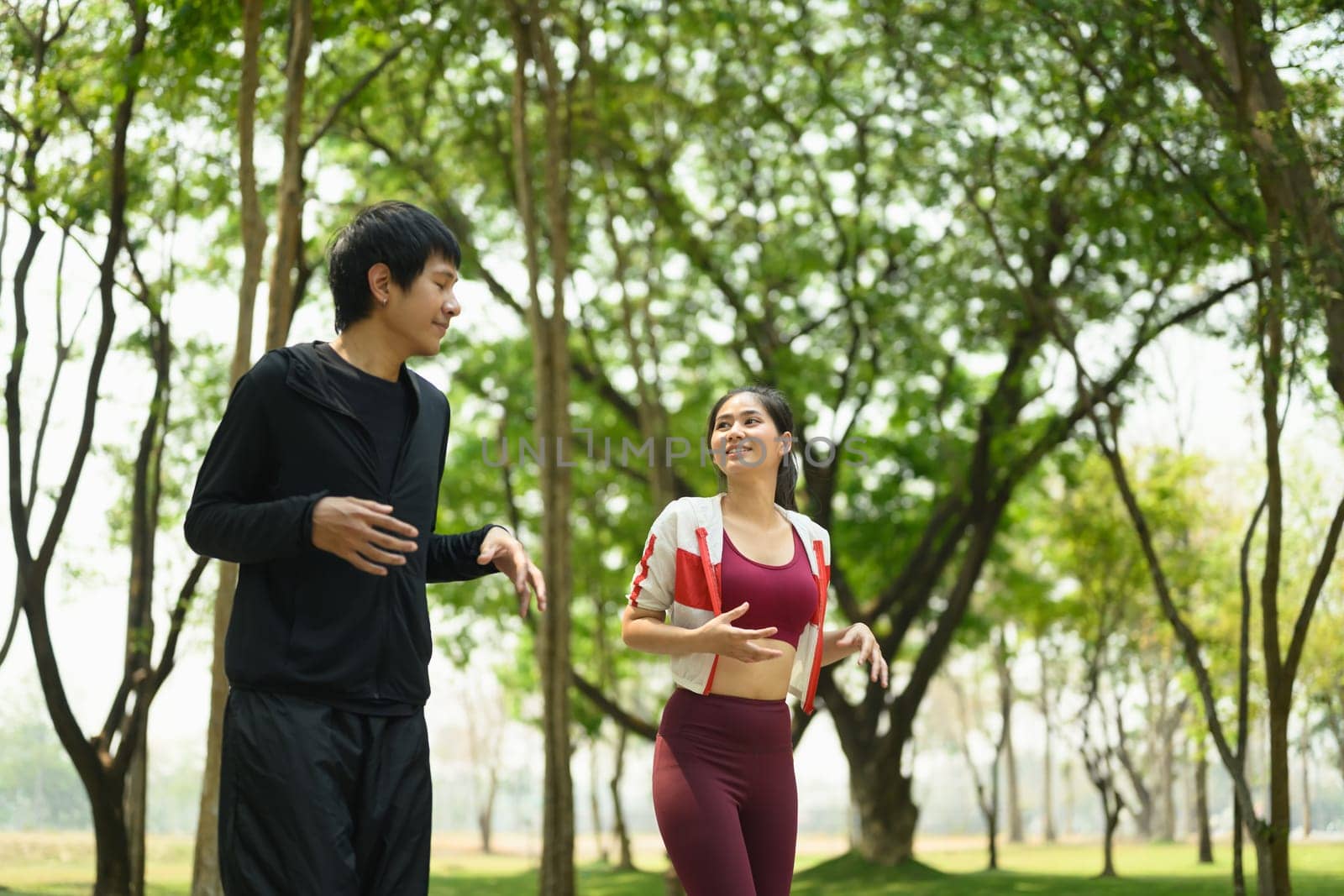 Cheerful young couple warming up before morning workout in a park.