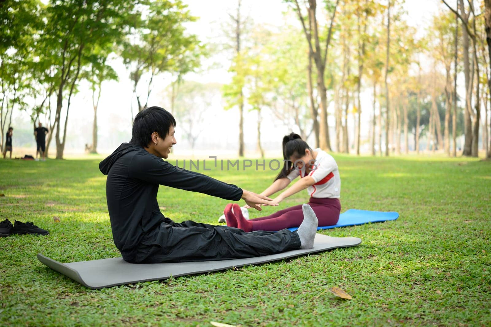Young man and woman stretching together on yoga mats in a green park. Healthy lifestyle concept.