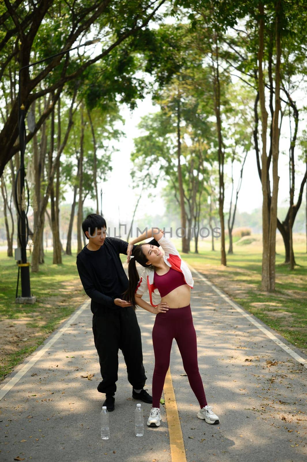 Athletic couple stretching together before a run on a sunlit park path.