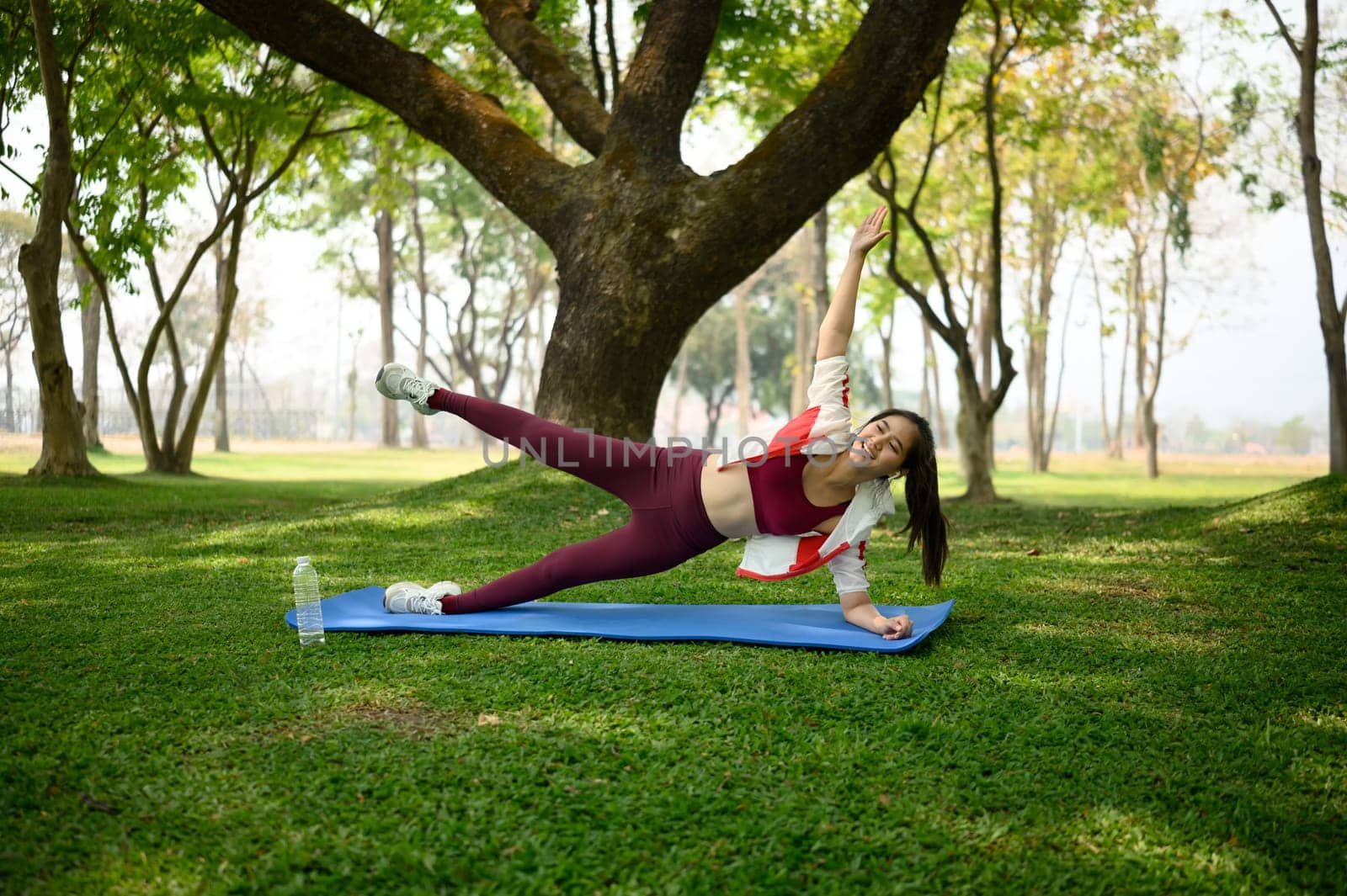 Fit woman doing side plank exercise on mat in the park.