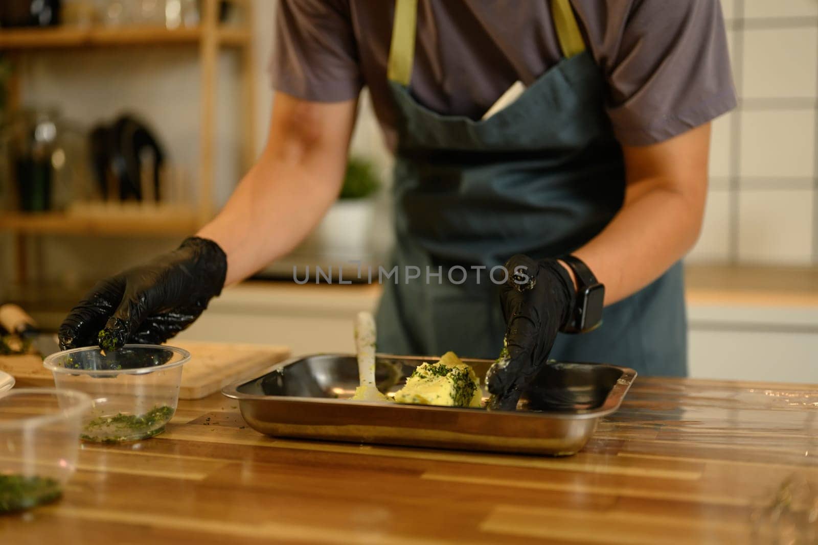 Man wearing black gloves mixing compound butter with fresh herbs and garlic on kitchen counter.