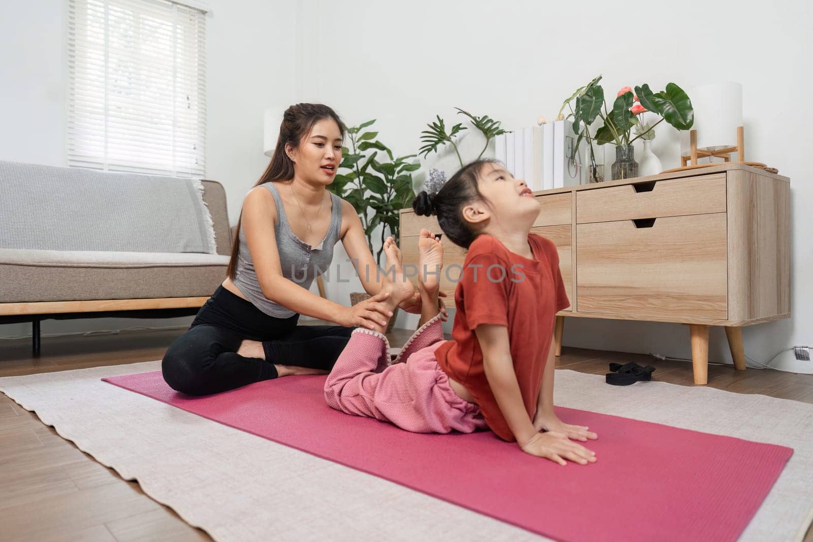 A nurturing yoga instructor supports a child as they practice the cobra pose, enhancing their flexibility and encouraging mindful movement in a serene home environment.