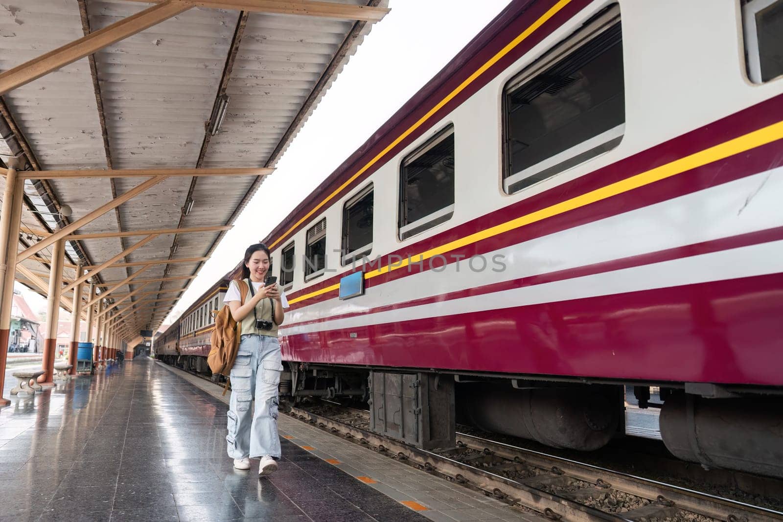 A young woman strolls along the platform, phone in hand and a determined smile on her face, ready to embark on her traveling journey.