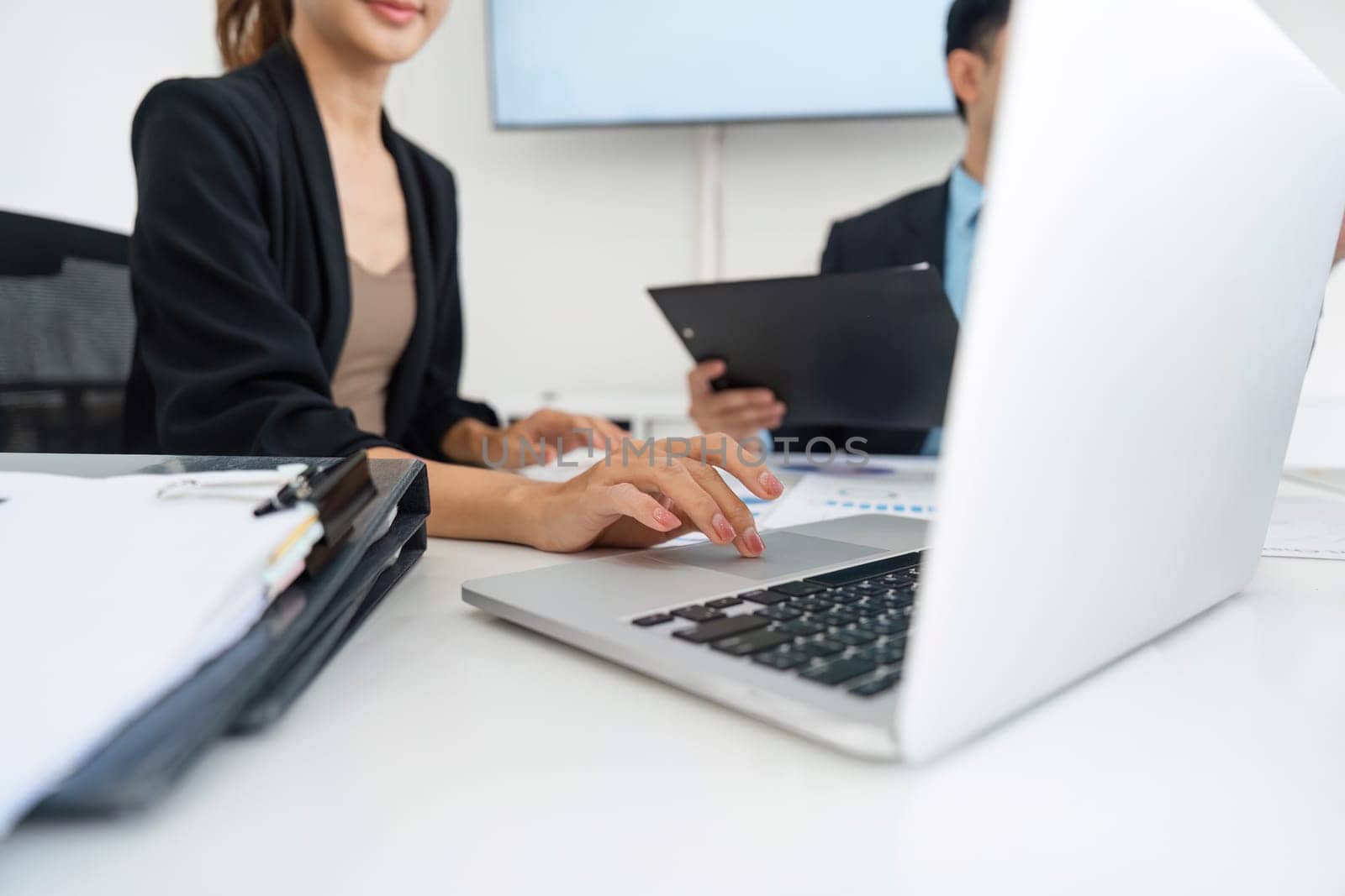 At a meeting table, one team member actively types notes and insights into a laptop during a collaborative discussion, highlighting the importance of technology in modern business.