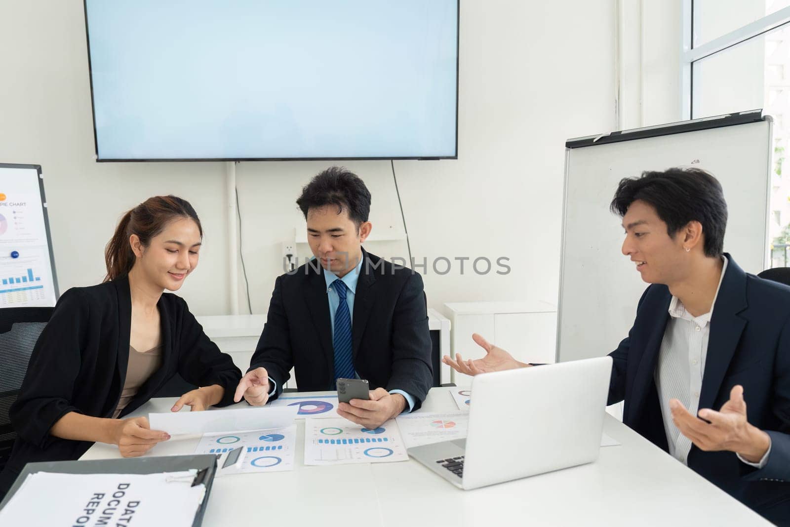 Team members engage in a lively discussion about project performance, analyzing data trends on their devices and papers during a strategy session.