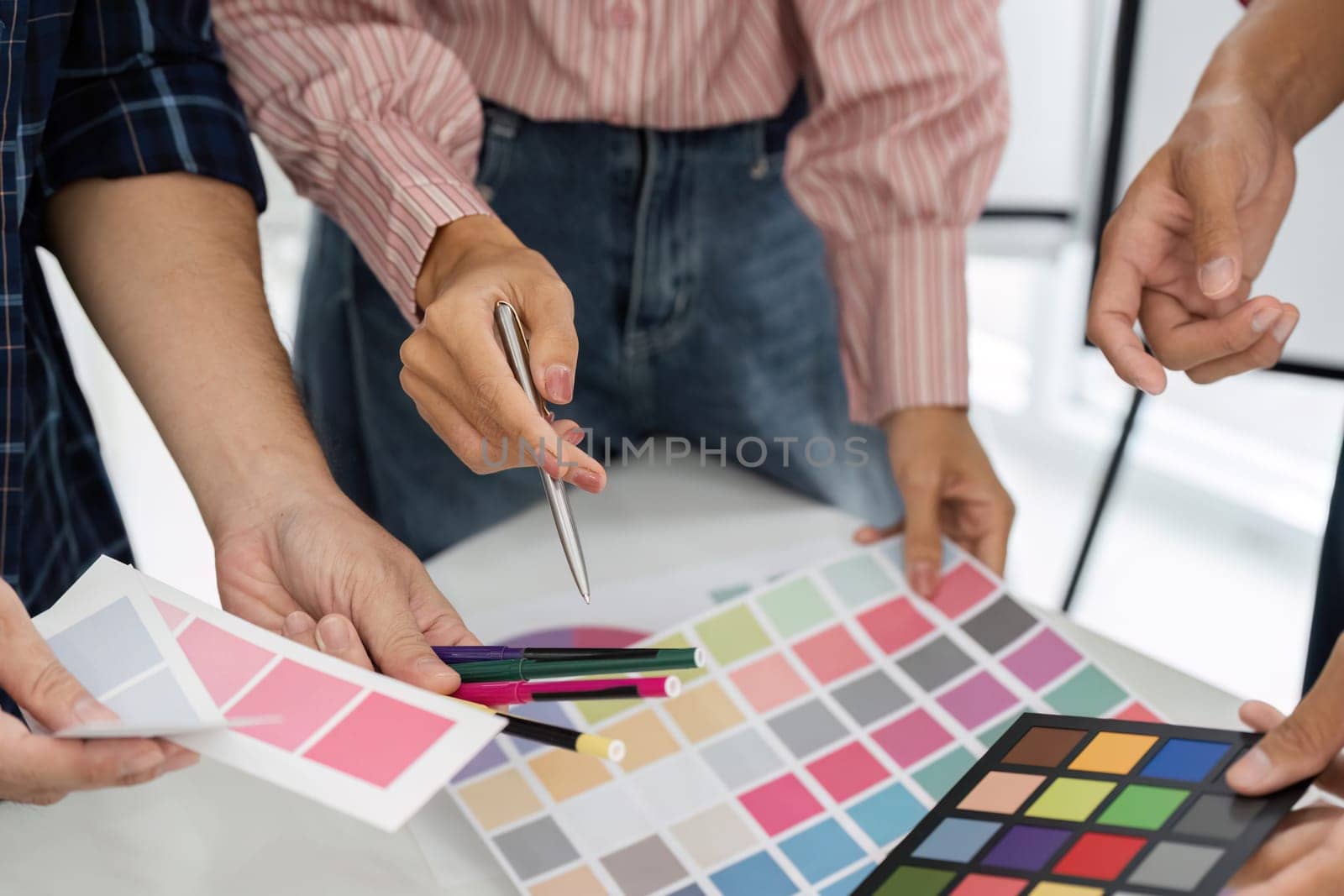 Team members enthusiastically discuss and choose color palettes from a variety of samples laid out on the table, blending ideas for their upcoming design.