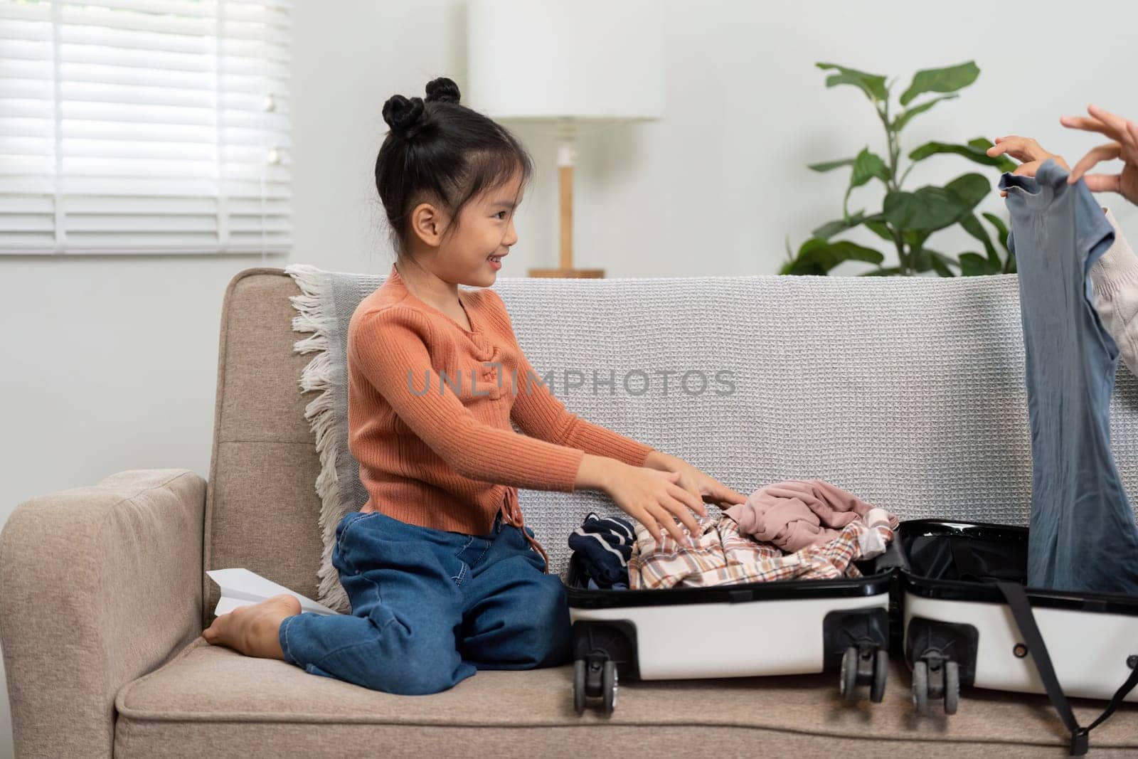 A joyful scene of a little girl assisting in packing a suitcase, showcasing family bonding and excitement for an upcoming journey. The activity highlights teamwork in travel preparation.