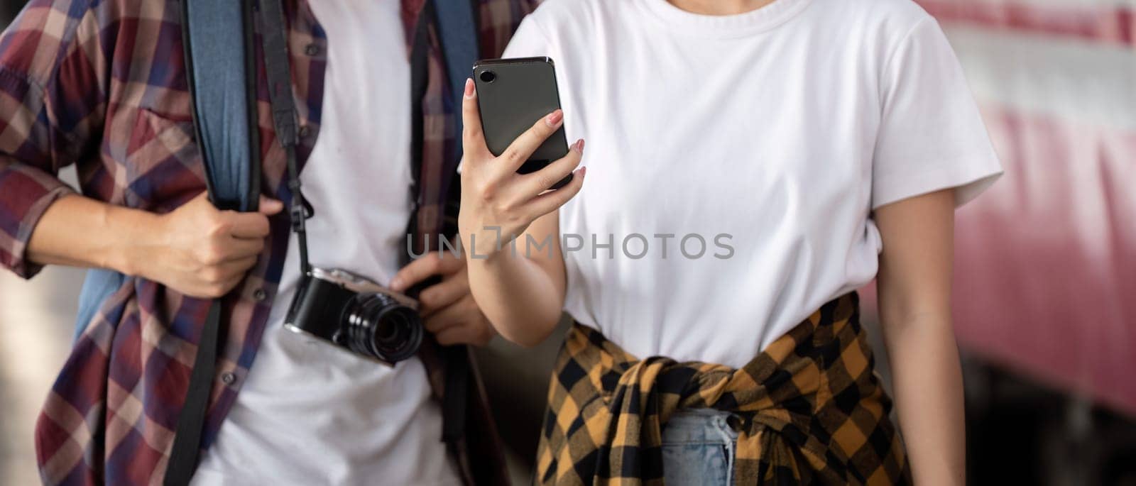 In a vibrant train station, a couple stands next to their bags as they admire travel memories captured on their smartphone, smiling and sharing stories.