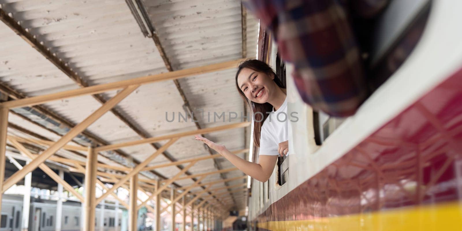 A cheerful traveler expresses her excitement while peering out of a train window, signaling her readiness for a new journey. The bustling station adds to the travel atmosphere.
