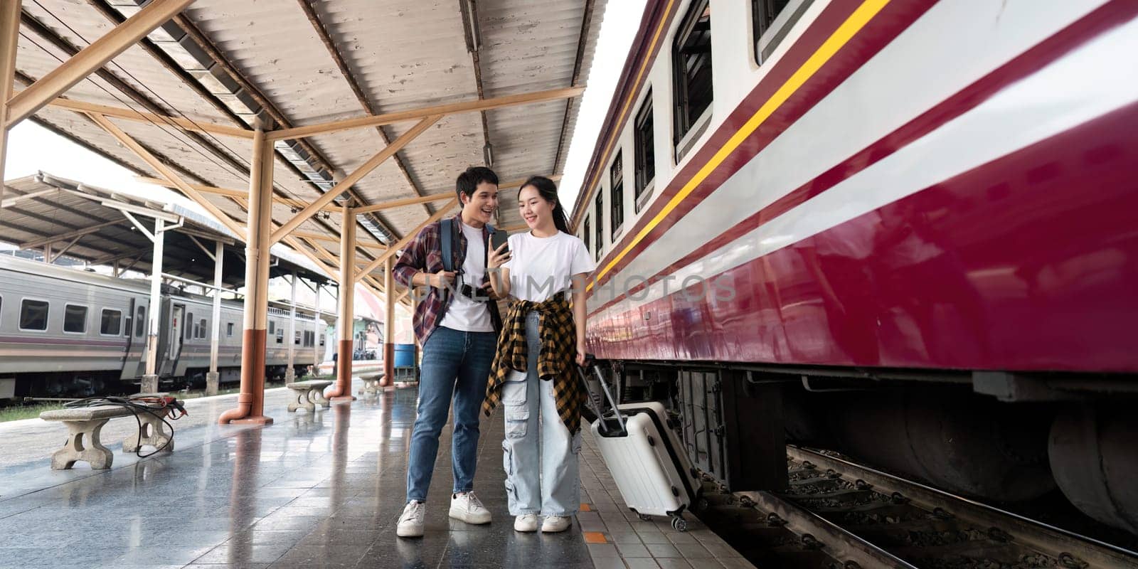 The couple stands side by side at the train station, laughing and enjoying a moment of connection as they await their train's arrival, showcasing a spirit of adventure.