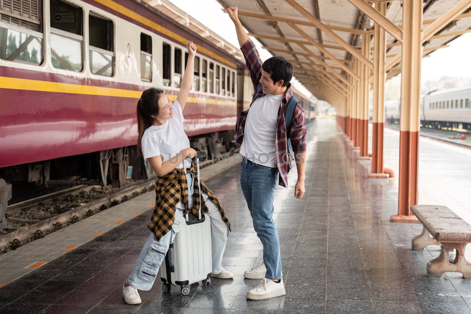 The couple expresses their excitement upon arrival at the destination with a joyful cheer at the train station, showcasing their travel triumph.